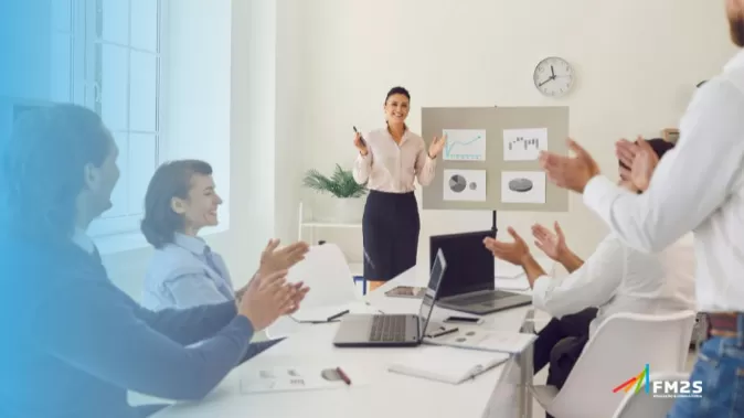 À esquerda degradê azul. Ao fundo, pessoas conversando em uma sala de reunião e uma pessoa em pé. No canto inferior direito, o logotipo da FM2S.